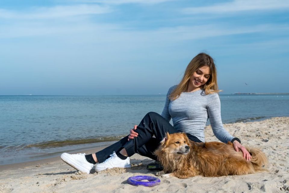 Woman enjoying a sunny day at Kołobrzeg beach with her dog, capturing a perfect seaside moment.